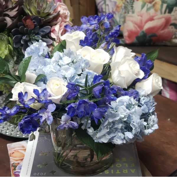 Blue hydrangeas, white roses, and purple flowers in a glass vase