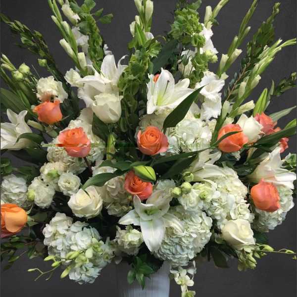 Large white floral arrangement with orange roses in a white vase