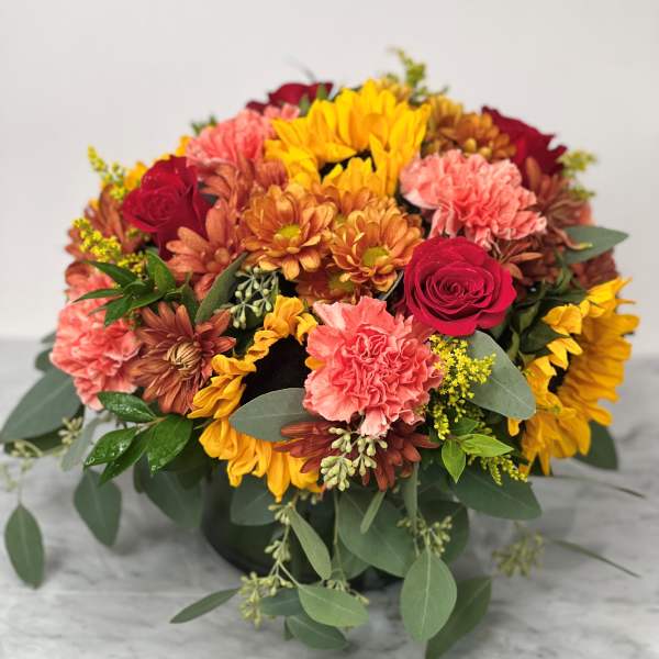 Mixed bouquet of sunflowers, roses, and carnations in a low container