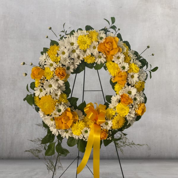 Yellow and white floral wreath on a black stand with a ribbon