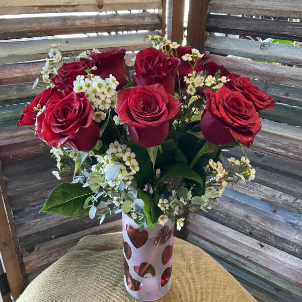 Red roses in a heart-cutout vase with small white filler flowers