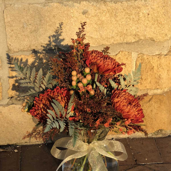 Orange chrysanthemum bouquet in a glass vase with a gold ribbon