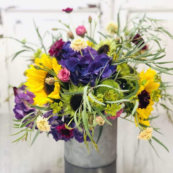 Mixed bouquet with sunflowers, purple hydrangea, and pink blooms in a gray vase