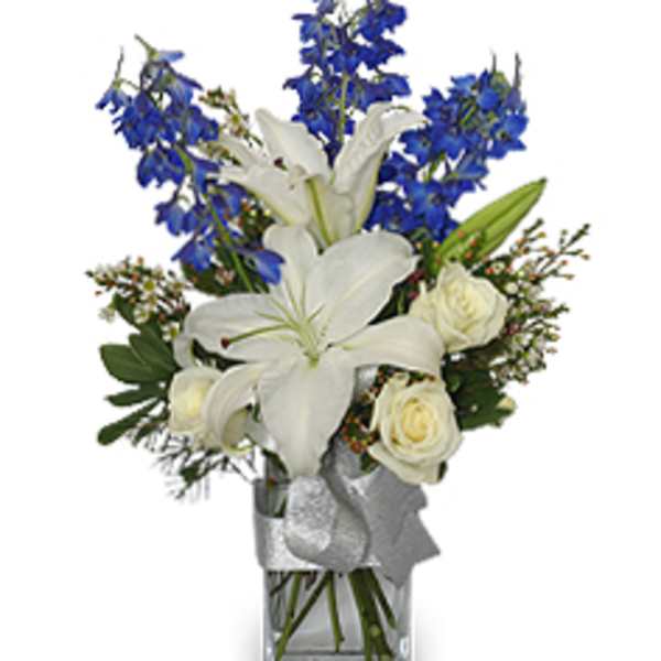 White lilies and roses in a clear glass vase with blue flowers
