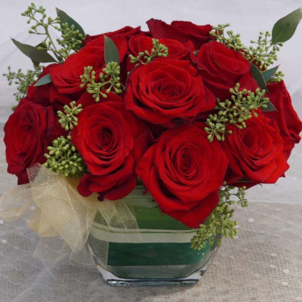 Red roses arranged in a square glass vase with a sheer ribbon bow