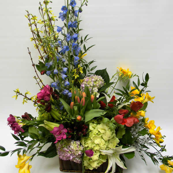 Tall mixed flower arrangement with blue, yellow, pink, and green blooms in a container