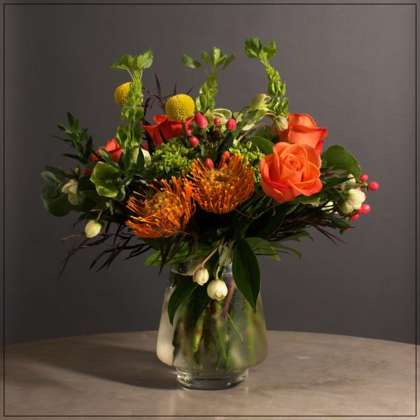 Orange roses and yellow pincushion blooms in a glass vase