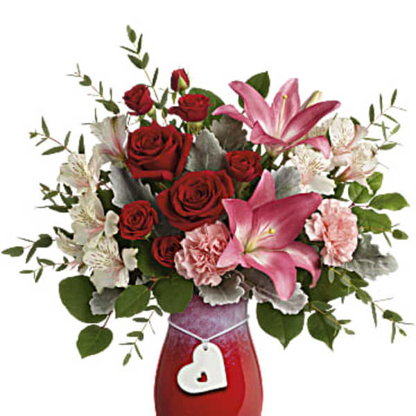 Red roses and pink lilies in a red vase with a heart charm