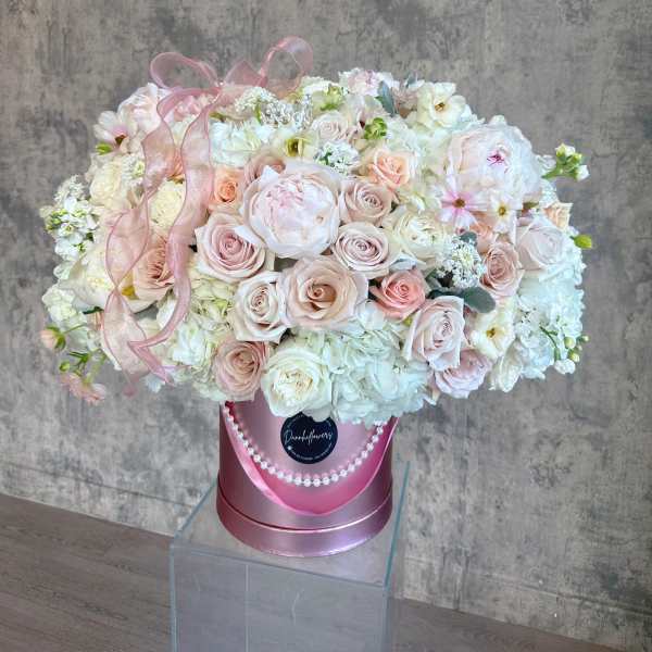 Large pastel bouquet of roses and white blooms in a pink hatbox