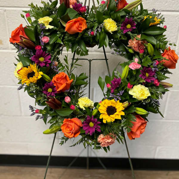 Heart-shaped floral wreath with orange roses and mixed blooms on a metal stand