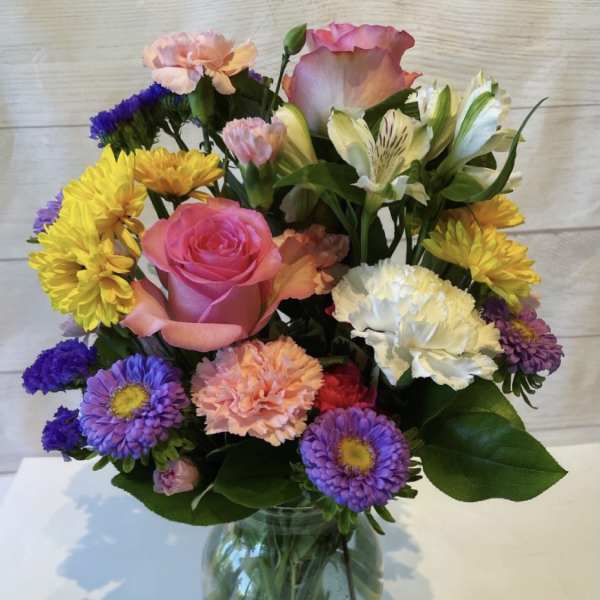 Mixed bouquet of pink, yellow, purple, and white flowers in a glass vase