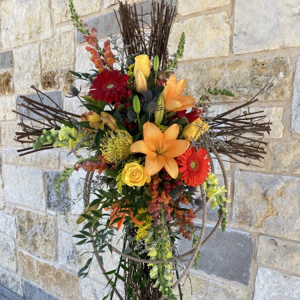Tall floral cross with orange and red flowers on a stand