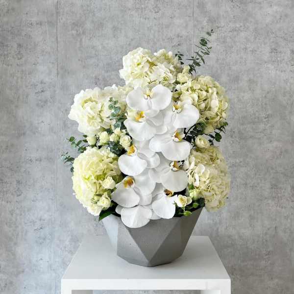 White orchids and pale hydrangeas in a gray geometric vase