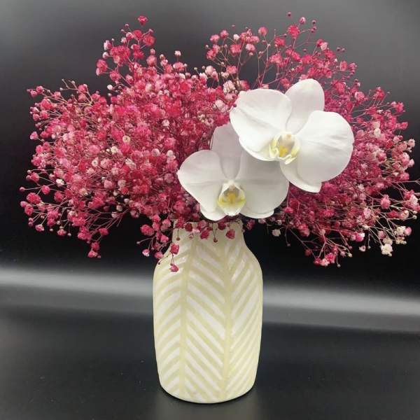 White orchids in a patterned vase surrounded by pink baby's breath