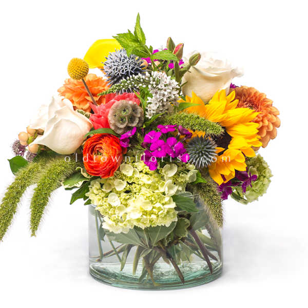 Mixed bouquet in a clear glass vase with sunflowers, roses, and hydrangeas