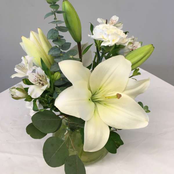 White lilies and alstroemeria arranged in a glass vase.