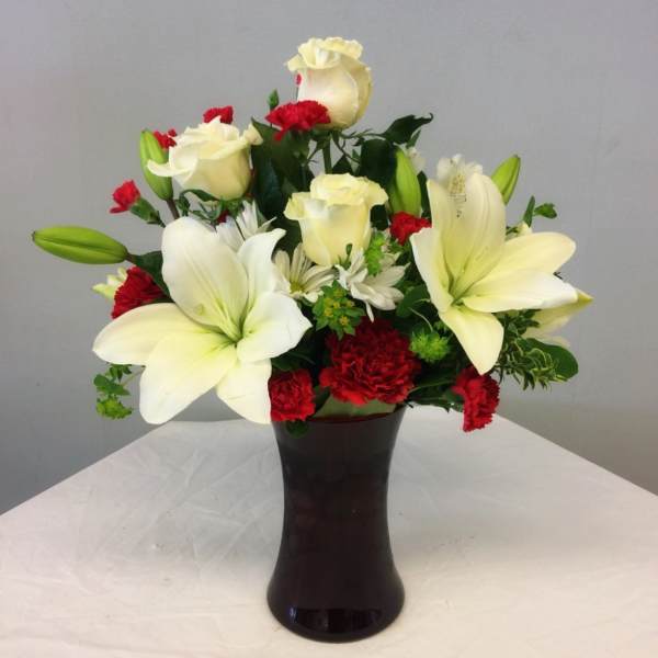 White lilies and roses with red carnations in a dark vase