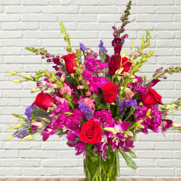 Bouquet of red roses, purple orchids, and pink snapdragons in a glass vase