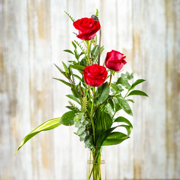 Red roses in a tall clear vase with scattered heart confetti