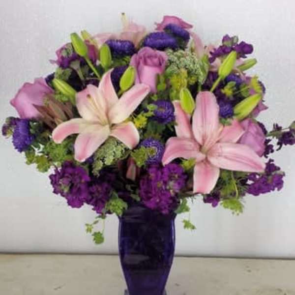 Pink lilies and purple flowers arranged in a tall purple vase