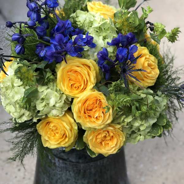 Yellow roses with blue flowers in a dark vase