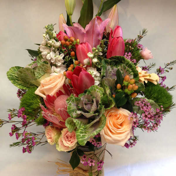 Mixed bouquet with pink lilies, roses, and tulips in a wrapped vase