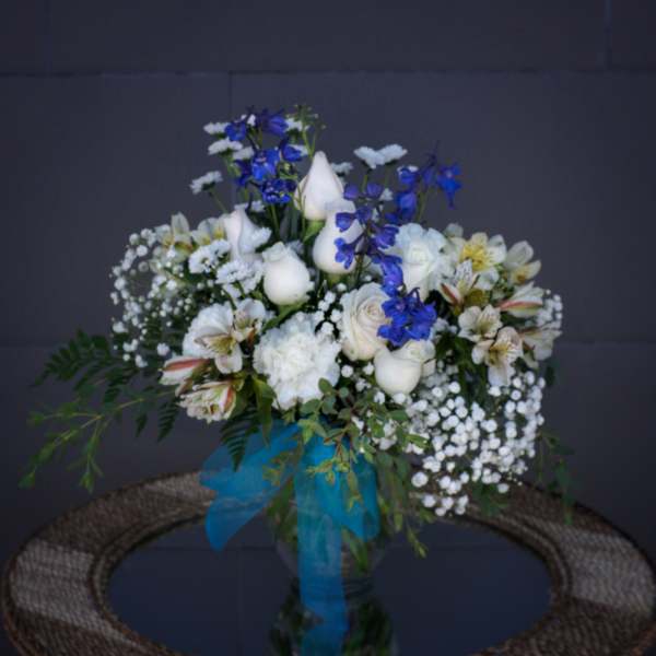 White and blue floral arrangement in a glass vase with a blue ribbon
