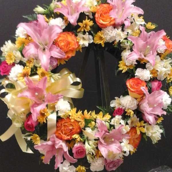 Heart-shaped floral wreath with pink lilies, orange roses, and white daisies