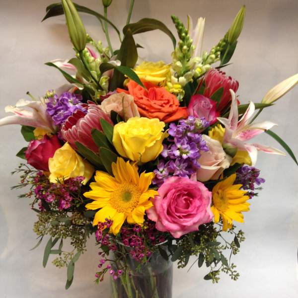 Mixed bouquet in a glass vase with roses, lilies, and sunflowers