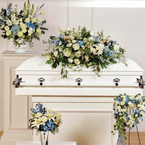 White casket with blue and cream floral sprays and arrangements