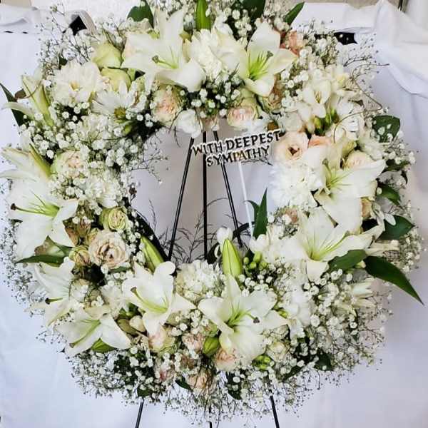 White sympathy wreath on a black stand with lilies and roses