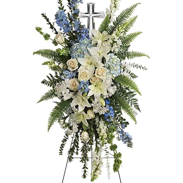 Standing floral spray with white lilies, cream roses, and blue flowers on an easel