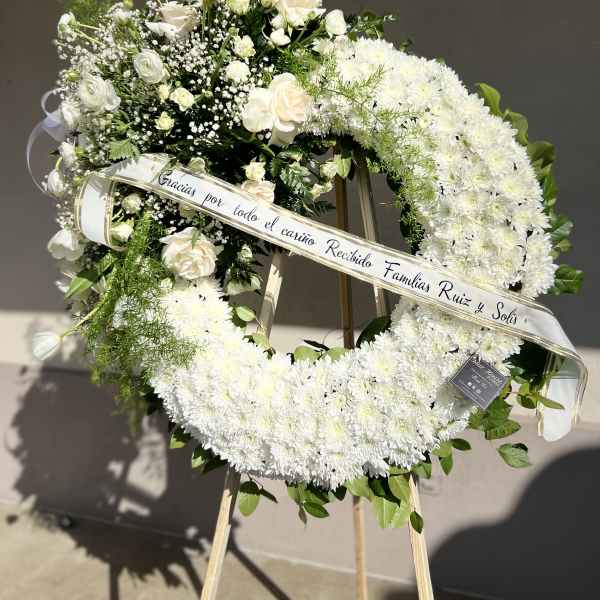 White floral funeral wreath on an easel with a ribbon banner
