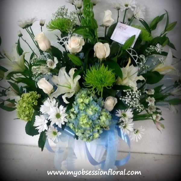 White roses and lilies with green and blue flowers in a ribboned bouquet