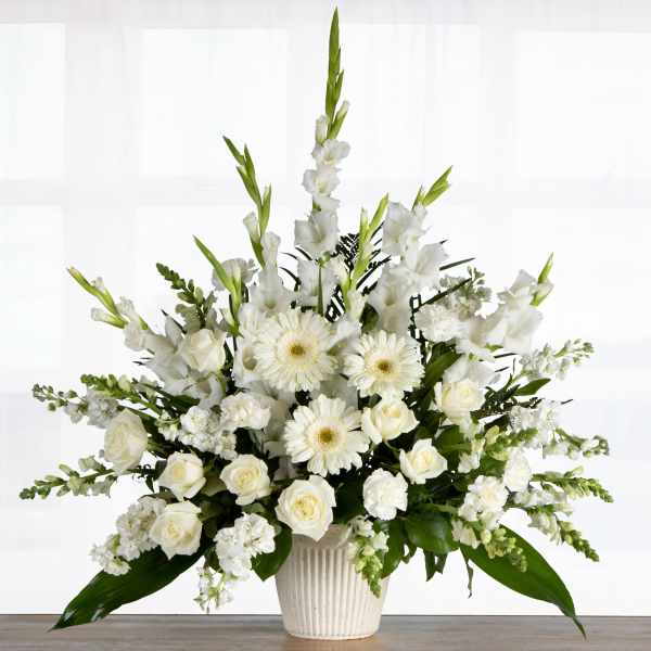Tall white arrangement of roses, gerbera daisies, and other blooms in a ribbed white pot