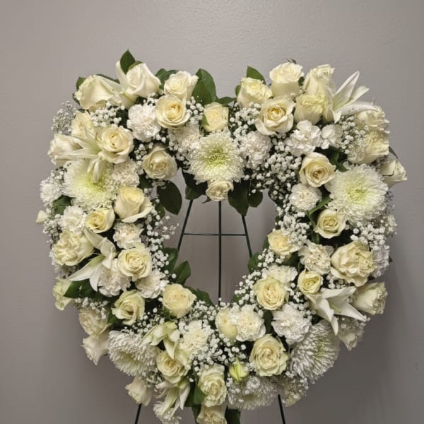 Heart-shaped standing wreath of white roses, lilies, and mums on a metal easel.