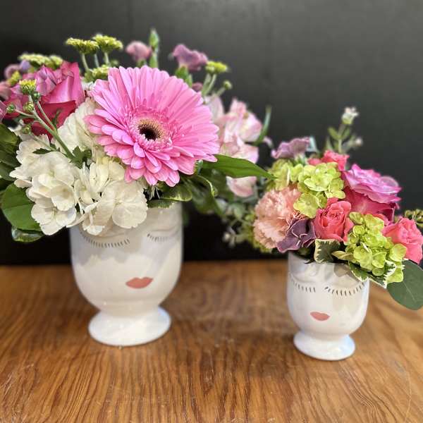Two floral arrangements in white face vases on a wooden table