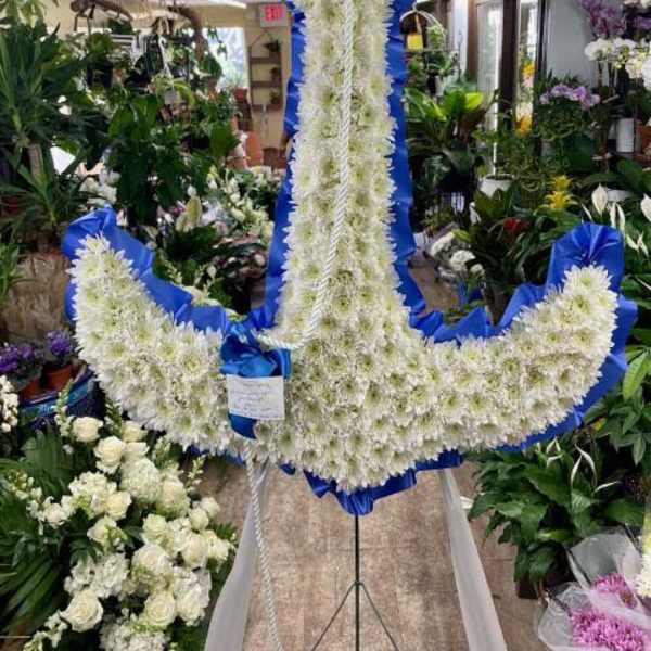 Large white floral anchor wreath with blue ribbon trim on a stand