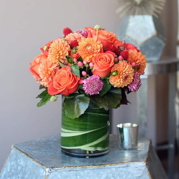 Orange roses and dahlias in a green glass vase