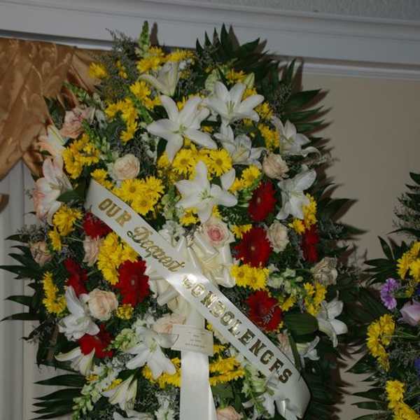 Large funeral wreath with white lilies, yellow daisies, and red flowers