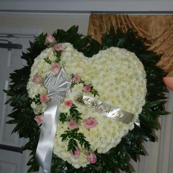 Heart-shaped white floral wreath with pink roses and a silver ribbon