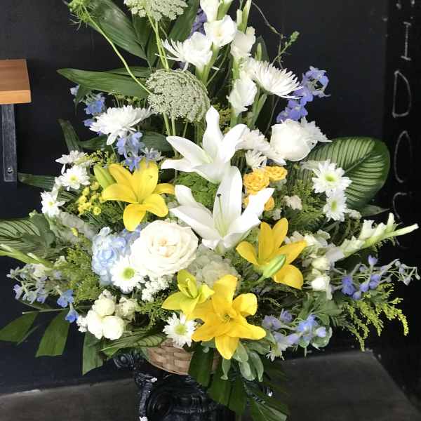 Large mixed floral arrangement with white lilies, yellow lilies, and blue flowers