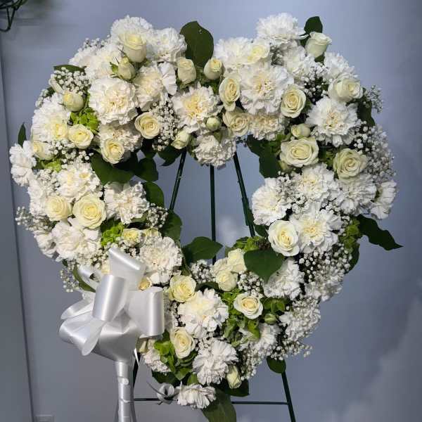 Heart-shaped white floral wreath on an easel with a silver bow