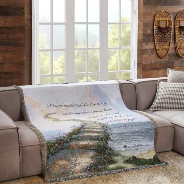 A decorative throw blanket with a seaside staircase scene and cursive text draped over a sofa