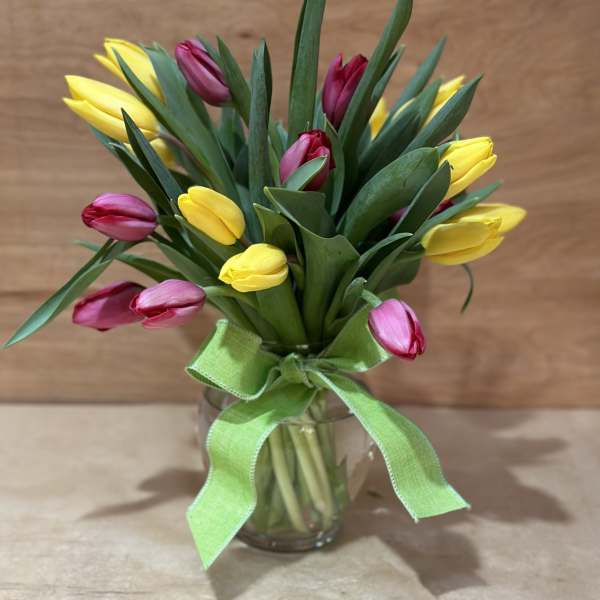 Bouquet of yellow and pink tulips in a glass vase with a green ribbon