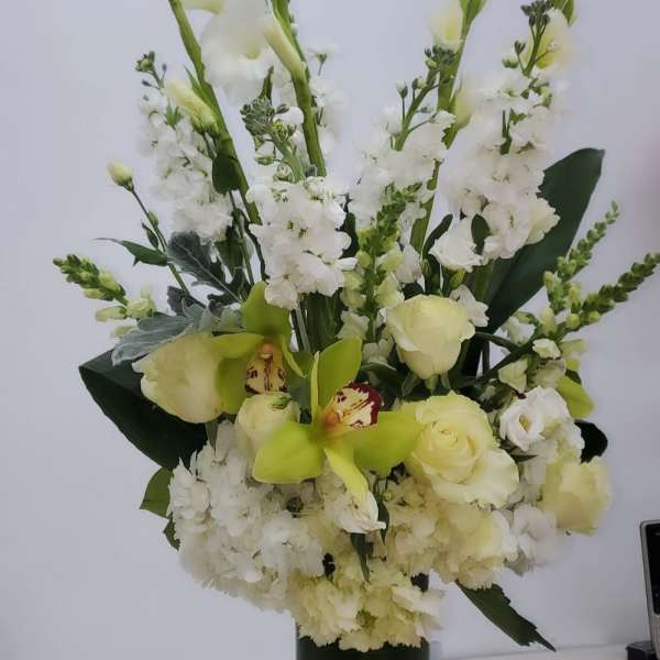 Tall white floral arrangement in a dark green vase with pale green orchids and roses