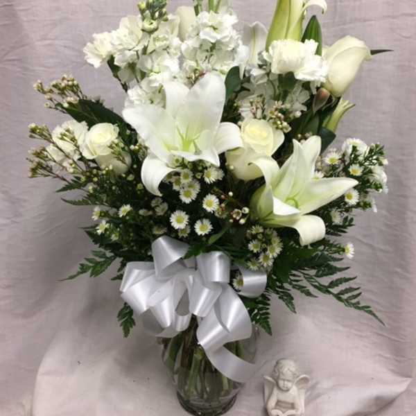 White lilies and roses in a glass vase with a white ribbon