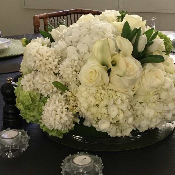 White floral centerpiece with roses and hydrangeas on a dining table