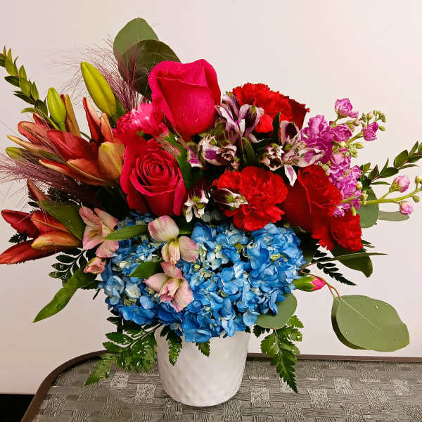 Colorful mixed bouquet in a white vase with blue hydrangeas and red roses