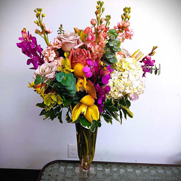 Tall mixed bouquet in a clear glass vase with roses, orchids, and hydrangeas